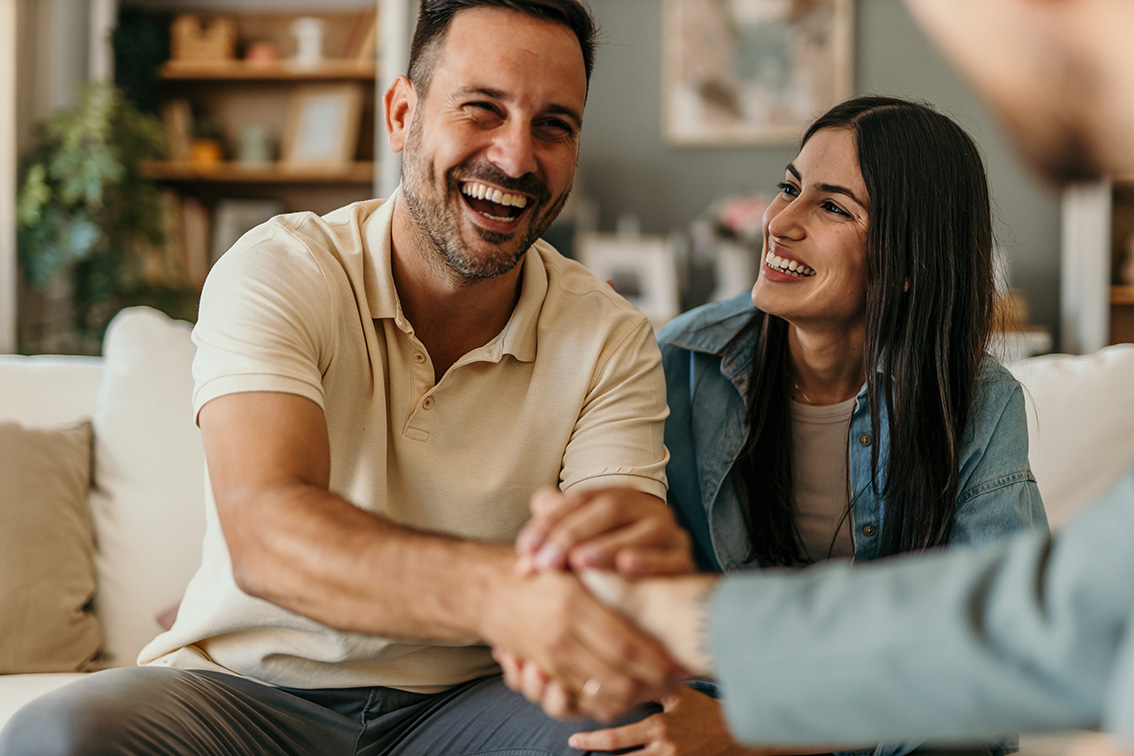 Happy couple shaking hands with financial advisor during meeting at home